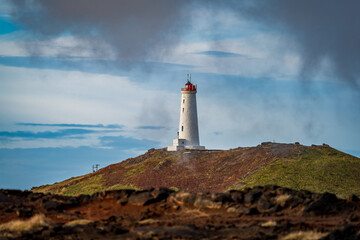 Fototapeta na wymiar Lighthouse over the volcanic landscape and dark cloudy sky