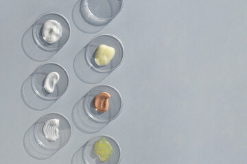 Multicolored texture of cream, scrub, serum, oil and hyaluronic acid in Petri dishes on a gray background. Concept of cosmetics laboratory researches. Smear of skincare cosmetics product.