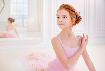 Obraz na płótnie Canvas Little ballerina girl in a pink tutu and pointe shoes posing in white studio
