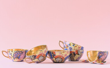 Vintage patterned teacups with a golden center on a pink background. One of them is broken. Copy space.