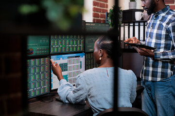 Investment company employees sitting at multi monitor workstation while analyzing real time trend...
