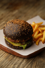 Black burger and french fries on wooden background