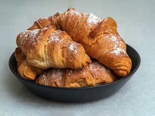 Homemade croissants on a dark plate sprinkled with powdered sugar