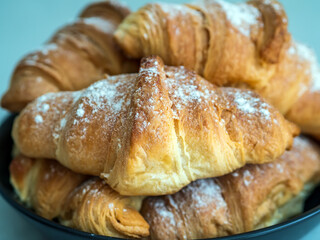 Homemade croissants on a dark plate sprinkled with powdered sugar