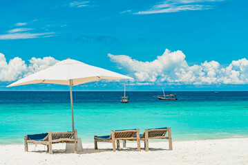 Wooden deck chairs on a sandy beach in front of ocean with boats, Zanzibar Tanzania