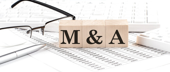 M and A written on wooden cube with keyboard , calculator, chart,glasses.Business concept