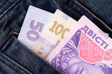 Ukrainian hryvnia protrude from the pocket of blue jeans close-up. Paper banknotes with a face...