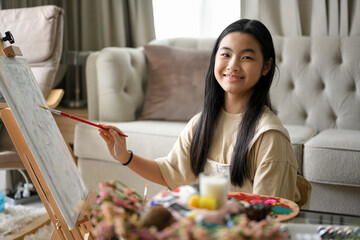 Creative asian young girl painting her beautiful artwork on canvas easel
