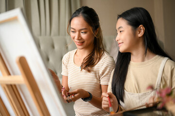 Woman enjoy painting the artwork on canvas easel with her younger sister