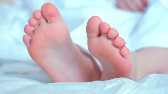 The bare feet of a child on white move. Fingers close up. Lazy morning, awakening.