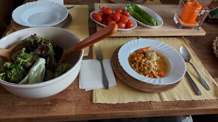 Gemüsesuppe auf einem weißen Teller. Karotten, Sellerie und Mais-Stücke in der Brühe. Besteck...
