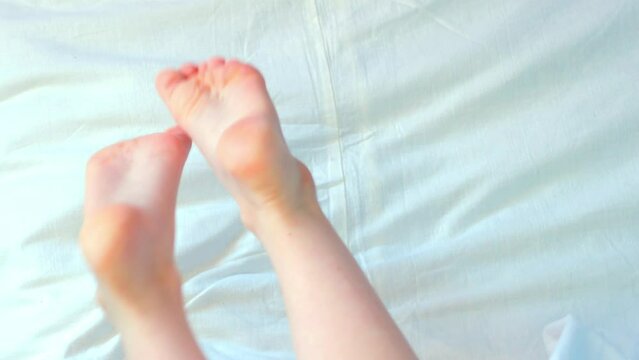The baby's bare feet are stretched on the white bed, then the baby rolls over from the top view.