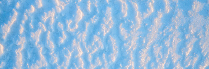 Beautiful winter background with snowy ground. Natural snow texture. Wind sculpted patterns on snow surface. Wide panoramic texture for background and design.