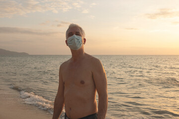 Senior man walking on beach in protective face mask