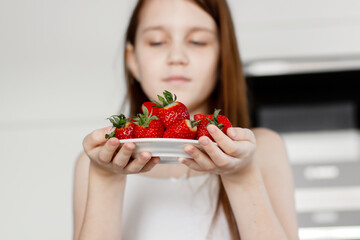 Preteen girl holding raw straberry, eating healthy food, drinking milk