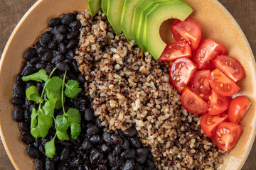 Vegan bowl with cooked beans, grains (brown rice, barley, quinoa) and raw vegetables (coriander, avocado, tomato). Top view.