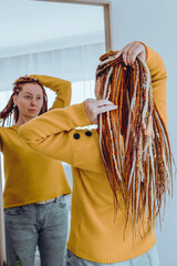 Woman with long red dreadlocks looks intently into a large mirror in her room.