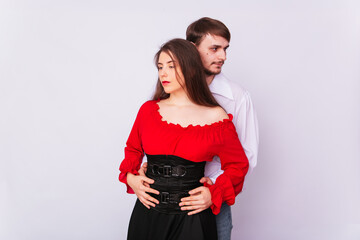 Young couple man and woman hugging on a white background. isolate. A handsome guy in a white shirt hugs a girl with long Spanish-style hair in a red peasant woman blouse and a black corset.