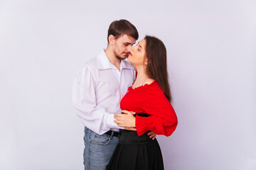 Young couple man and woman hugging on a white background. isolate. A handsome guy in a white shirt hugs a girl with long Spanish-style hair in a red peasant woman blouse and a black corset.