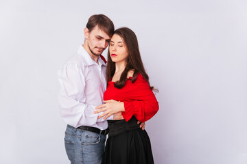 Young couple man and woman hugging on a white background. isolate. A handsome guy in a white shirt hugs a girl with long Spanish-style hair in a red peasant woman blouse and a black corset.