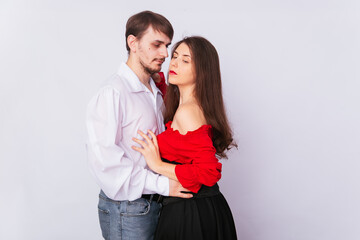 Young couple man and woman hugging on a white background. isolate. A handsome guy in a white shirt hugs a girl with long Spanish-style hair in a red peasant woman blouse and a black corset.