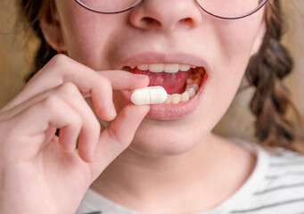 Ein Kind hält eine weiße Tablette und öffnet den Mund. Medikamente und synthetische Vitamine. Das Konzept der Drogenauswahl. Behandlung für Kinder.