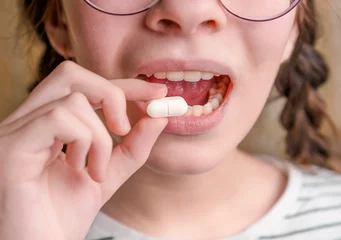 Foto op Plexiglas Lieve mosters Een kind houdt een witte tablet vast en opent de mond. Medicijnen en synthetische vitamines. Het concept van drugsselectie. Behandeling voor kinderen.