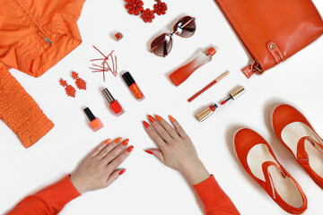 Women's hands with manicure and items of women's clothing and accessories in orange on a white background.