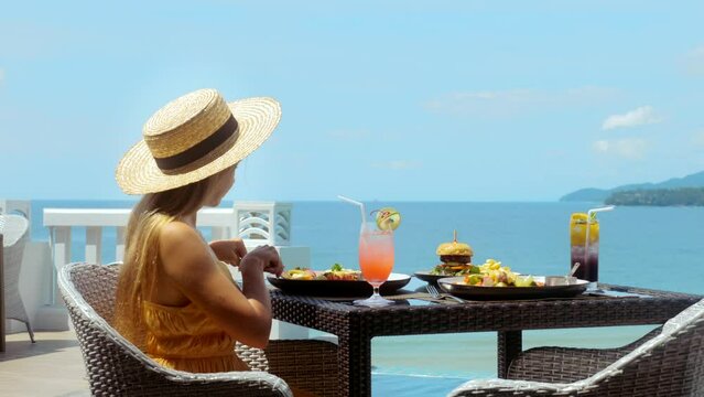 Young woman in straw hat, relax in luxury tropical resort, having breakfast in restaurant with sea view. Traveling through Asia. Traveler woman on weekend, tourist on summer vacation travel