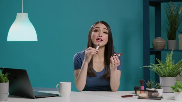 POV of asian influencer doing lipstick recommendation in studio, filming makeup review with cosmetics product on camera. Female blogger recording video for social media. Tripod shot.