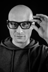 Portrait in black and white of a young bald man with black eyeglasses who with his hand adjusts them on his face