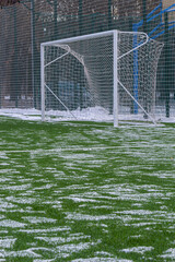 field for playing football in winter, artificial grass on cleared of snow in the distance gate and net