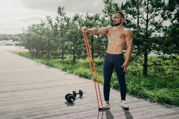 Strong sportsman flexes muscles with elastic resistance band, uses sport equipment for workout,...