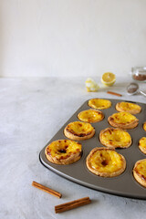 Portuguese custard tarts (pastel de nata or pastel de Belem) in the gray baking mold. With cinnamon sticks, lemon and cinnamon powder on the gray background.