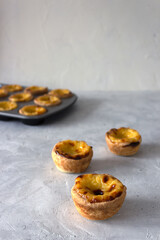 Pastel de nata or pastel de Belem, traditional portuguese dessert. Three tarts on the gray table and  the gray baking mold on the background. 