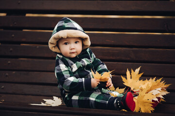 Adorable baby in warm overall with hood sitting on foliage.