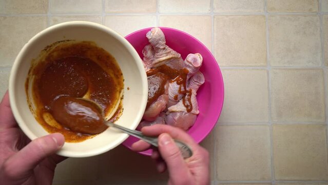 Marinating raw chicken legs in the home kitchen. Add a few tablespoons of sauce for cooking. Mixing ingredients. Culinary master class. Top view.