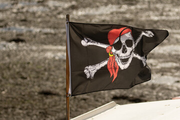 Fluttering Pirate Skull and cross bones flag on small boat in harbour