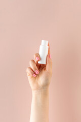 A woman's hand holds a white tube with a cosmetic product on a pink background. Beauty product concept. Sample.