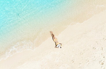 Fototapeta na wymiar Aerial view with Young woman in a yellow bikini lying on the back on the white sand with waves of turquoise blue sea background
