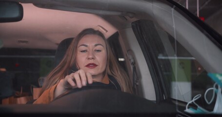 Fototapeta na wymiar Dealing with stress. Beautiful young blonde woman sits in car stuck in traffic jam, closing eyes and trying to breathe.