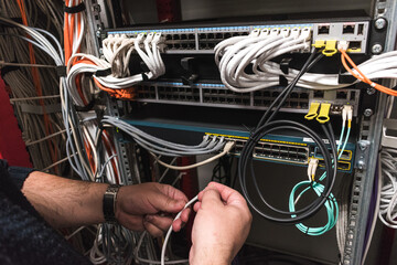  IT technician handling fiber optic cables from a communications cabinet