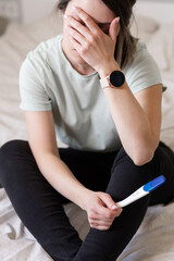 the woman found out about an unwanted pregnancy. A woman with a pregnancy test in her hands is sitting on the bed in her apartment