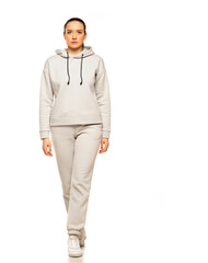 Front view of a young woman in a gray tracksuit and hood walking to a white background in the studio