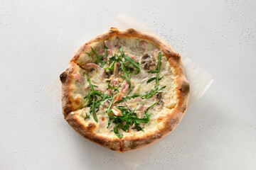 Freshly baked crispy pizza with bacon, ham, arugula and cheese on white background. Delivery food. View from above