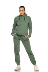 Fototapeta premium Front view of a young woman in a green tracksuit posing to a white background in the studio
