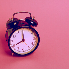 vintage old black alarm clock on pink background