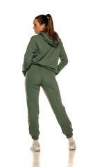 Fototapeta premium Rear view of a young woman in a green tracksuit posing to a white background in the studio