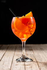 Glass of aperol spritz cocktail on wooden table and black background