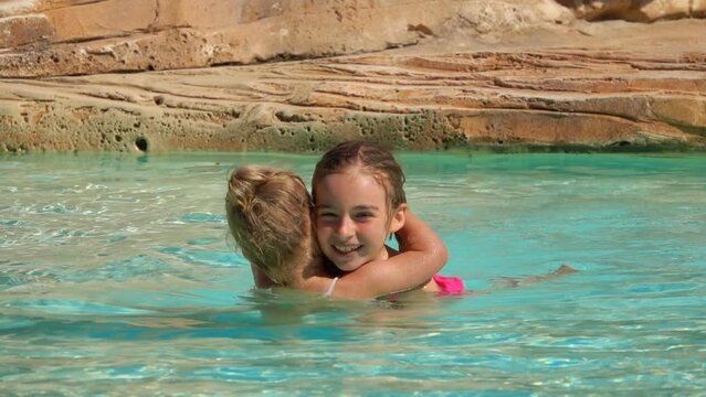 Two sibling girls are hugging in the swimming pool 